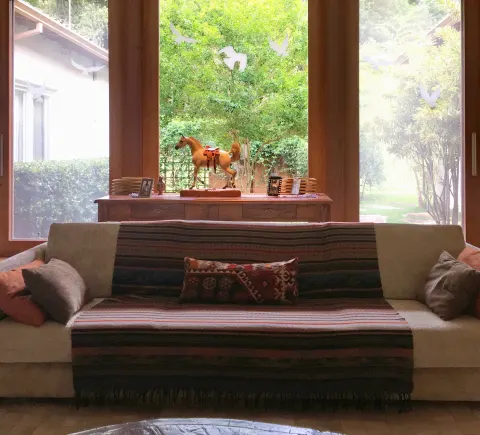 Sala com sofá coberto por manta listrada diante de janelas para o jardim