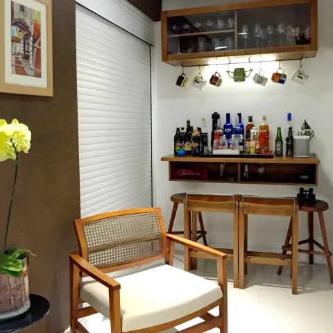 Canto de bar com banquetas de madeira, prateleiras e poltrona de palhinha