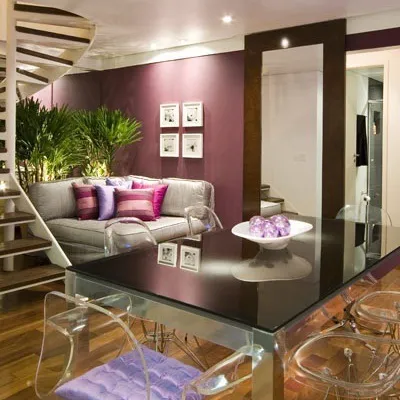 Sala com parede roxa, sofá com almofadas lilás e mesa de vidro