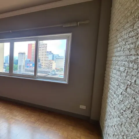 Sala vazia com piso de taco, parede de tijolinho branco e janela para a cidade