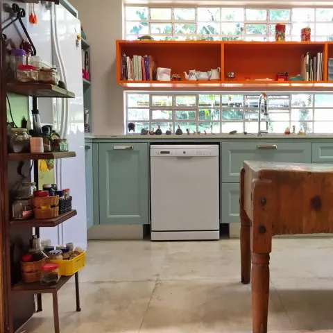 Cozinha com piso de cimento claro, armários verde-água e nichos laranja